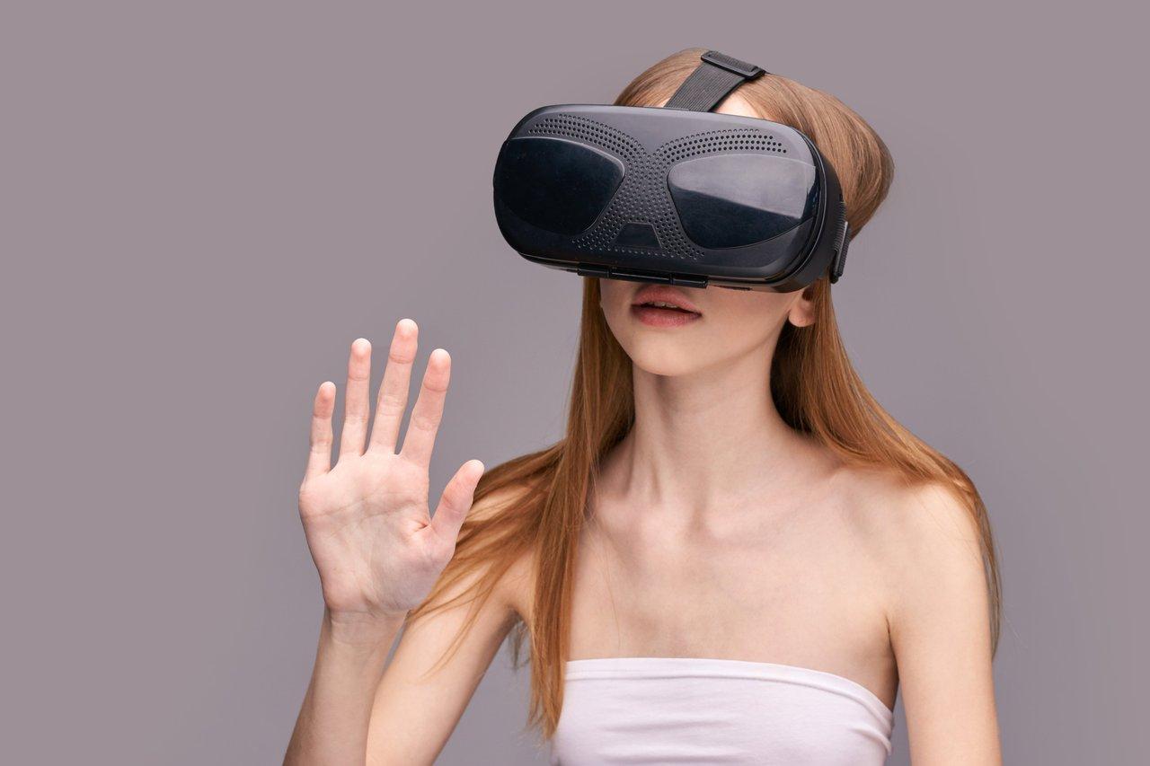 Jeune femme caucasienne utilisant un high-end VR AR headset avec gestes interactifs sur fond gris.
