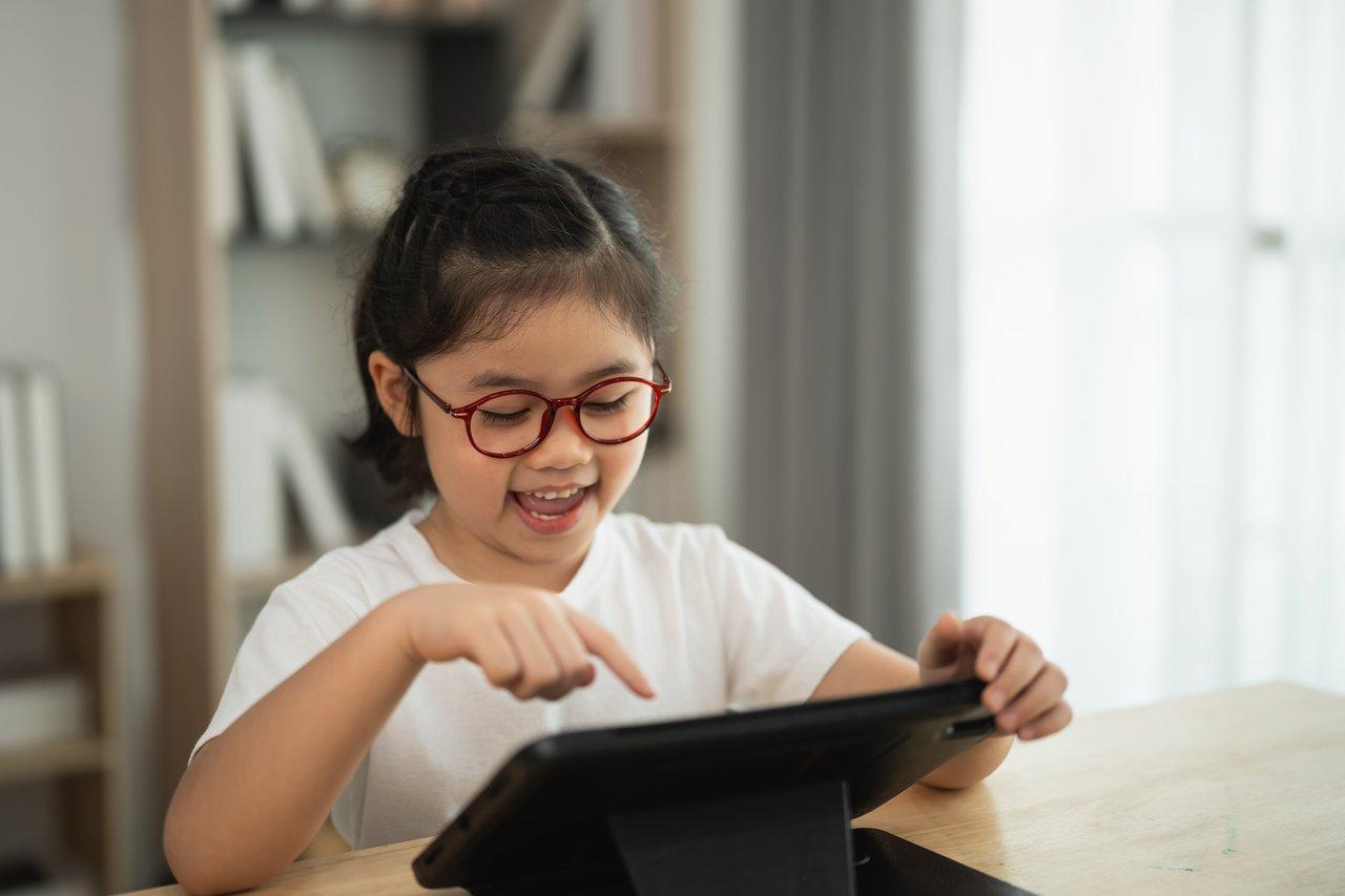 Jeune fille asiatique utilisant une application d'orthographe interactive sur tablette pour apprendre avec plaisir à la maison.